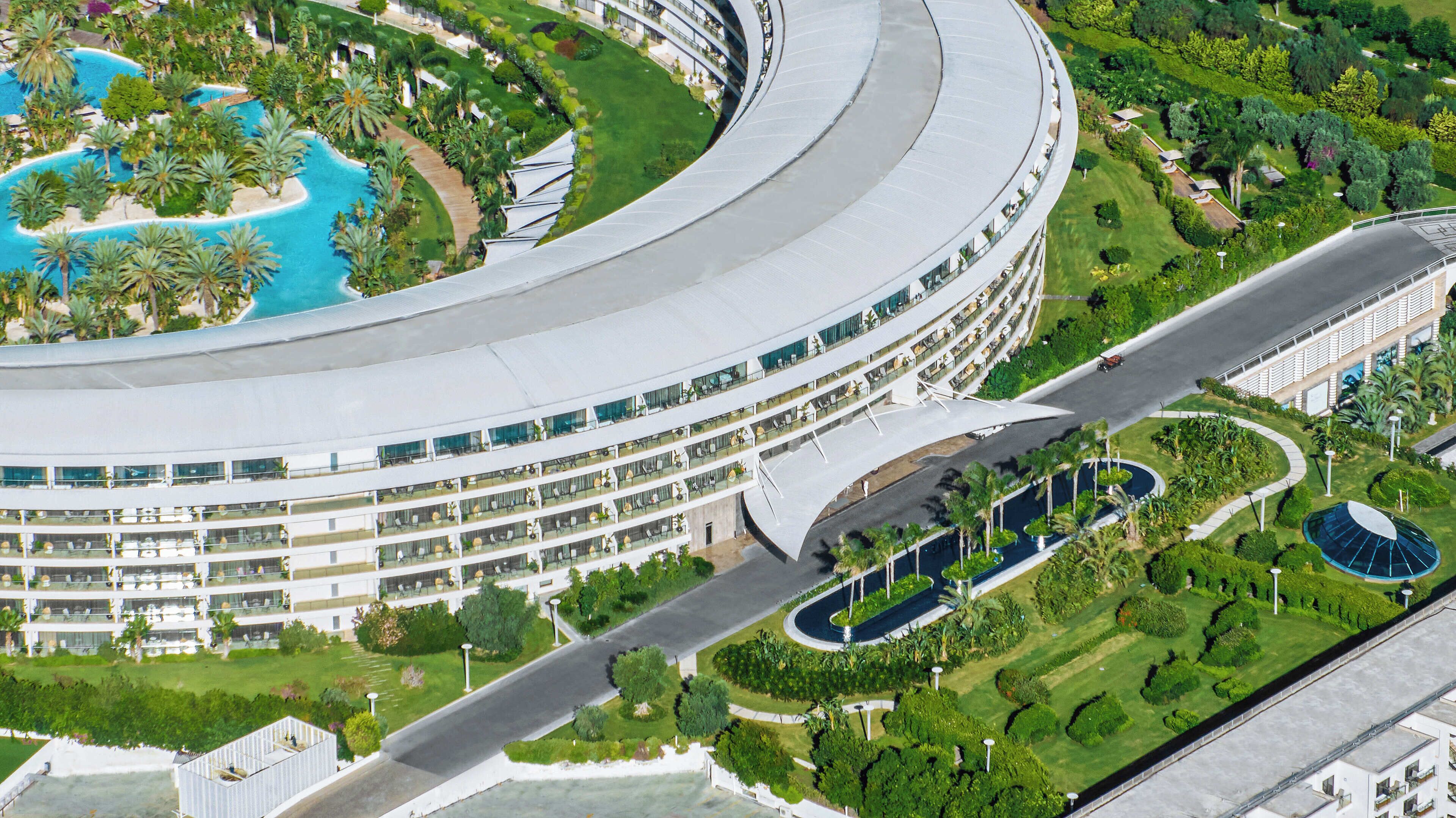A modern hotel with a curved facade, multiple balconies, and a central courtyard with a pool.