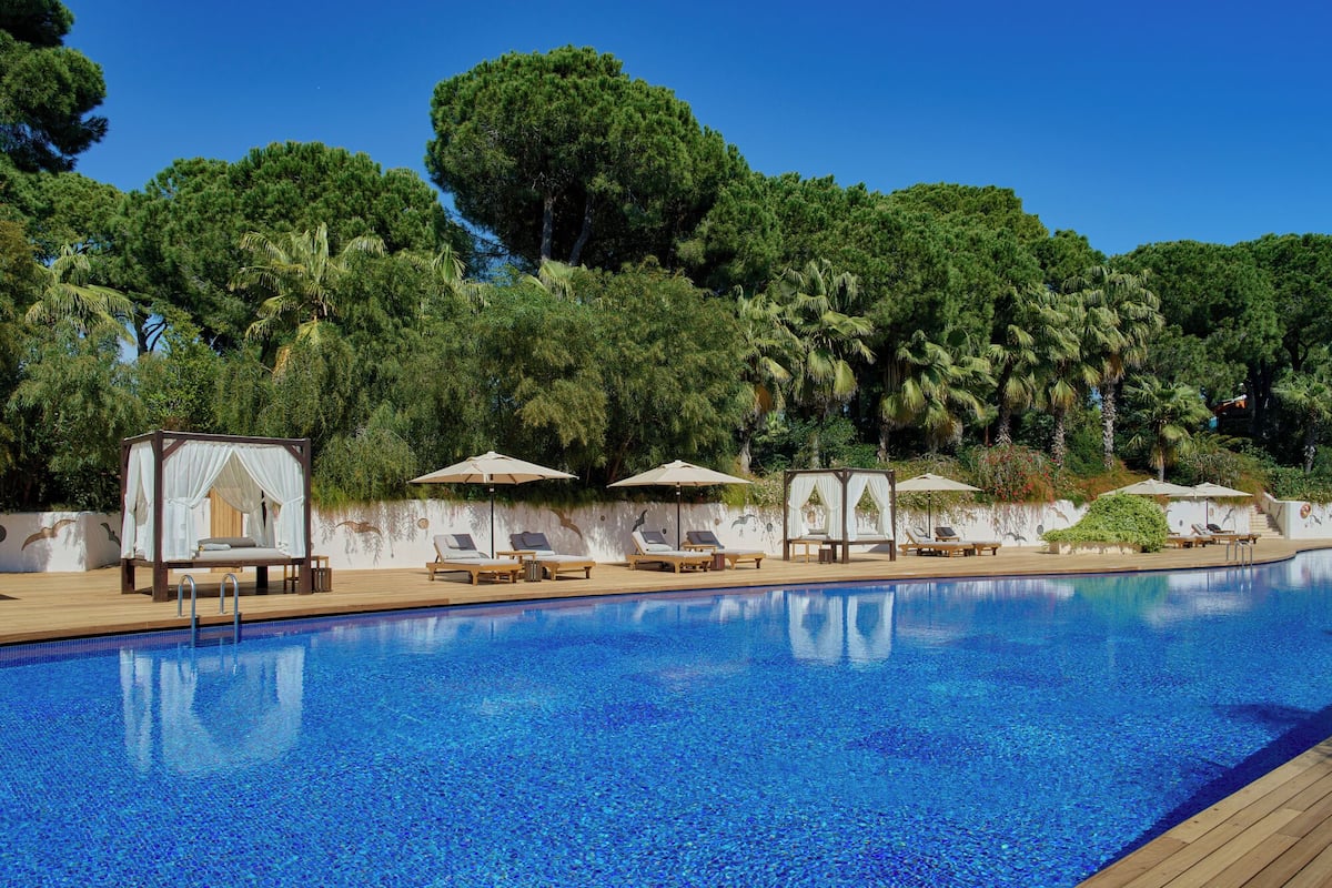 A pool area with lounge chairs and umbrellas, surrounded by lush greenery.