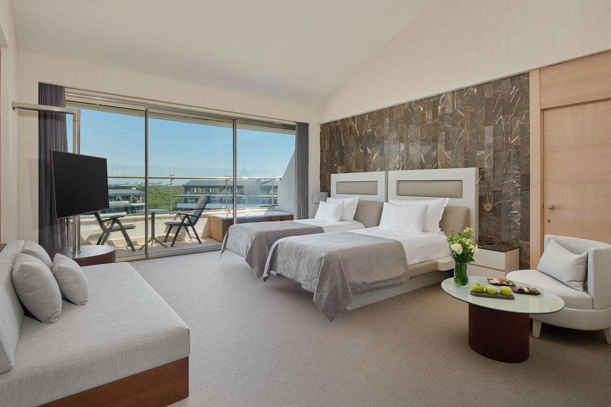 A modern hotel room with a large bed, a sofa, a small table, and a TV.