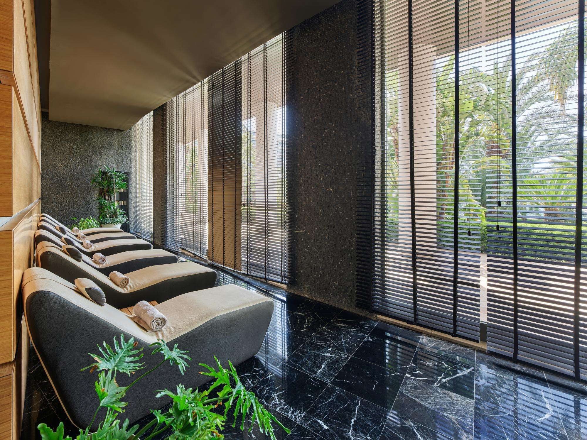 A modern spa area with massage chairs, a stone wall, and large windows with blinds.