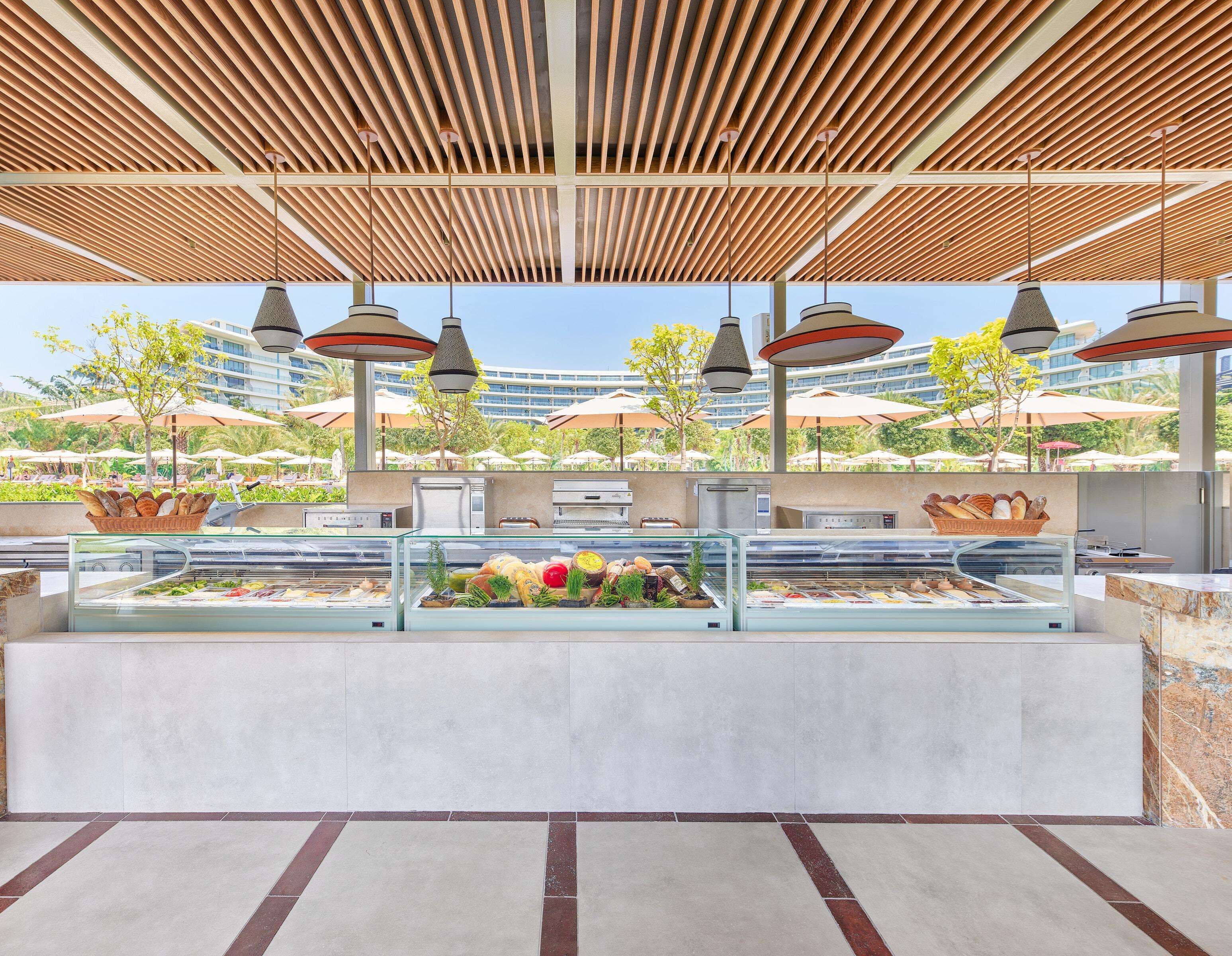 An outdoor buffet area with a modern design, featuring a wooden ceiling and multiple hanging pendant lights.