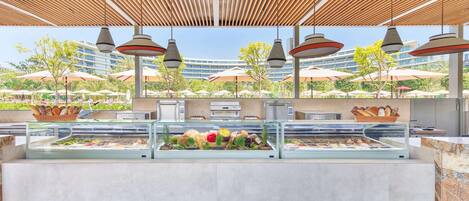 An outdoor buffet area with a modern design, featuring a wooden ceiling and multiple hanging pendant lights.