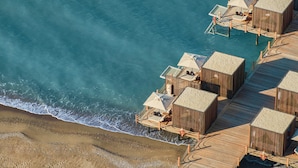 An aerial view of a beachside resort with wooden overwater bungalows connected by a wooden deck. - Maxx Royal Belek Golf Resort (Serik)