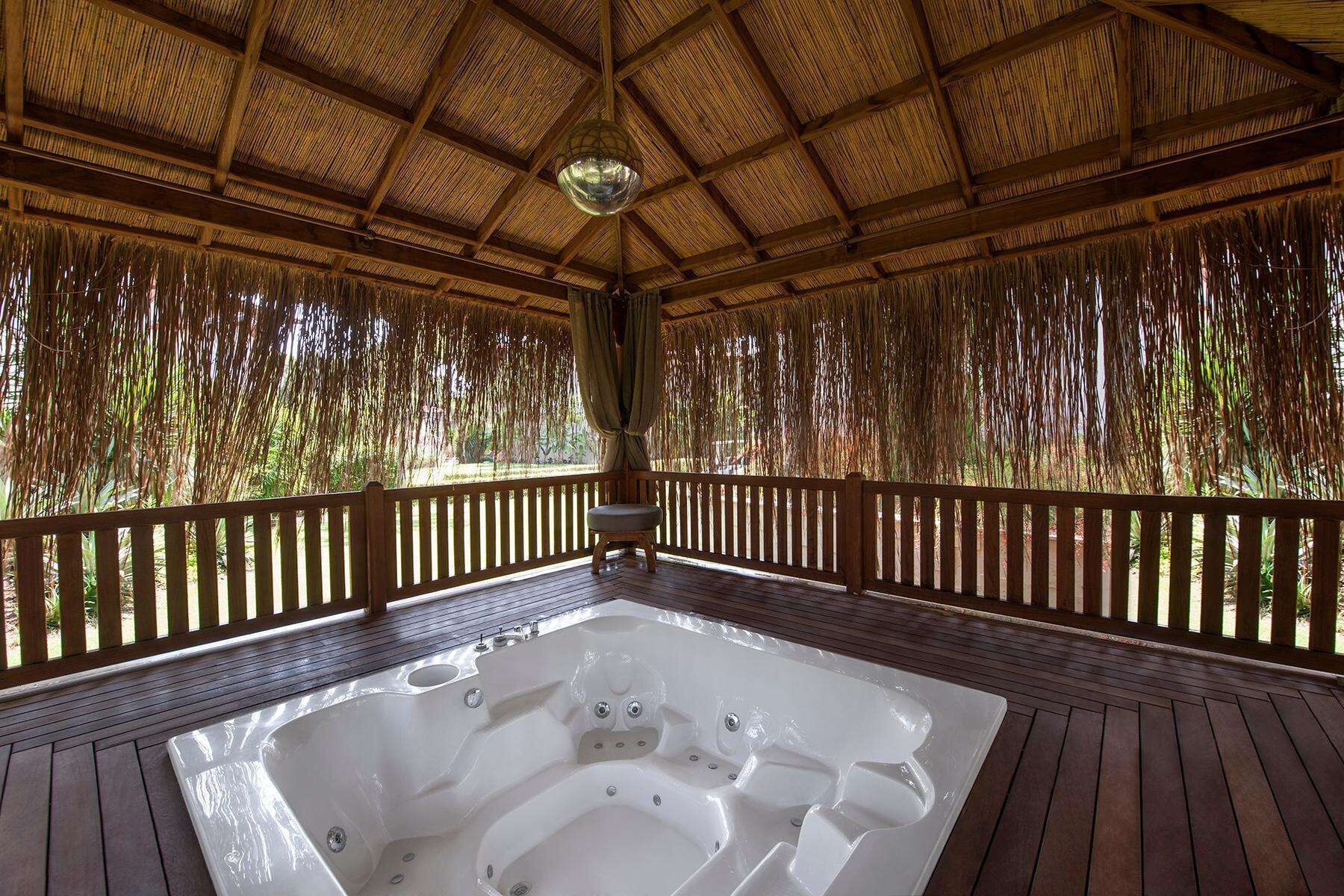 Un bain à remous situé dans un espace extérieur abrité, doté d’une terrasse en bois et d’un toit de chaume.