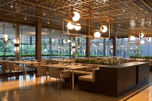 A modern restaurant with a spacious layout, large windows, and contemporary lighting fixtures.