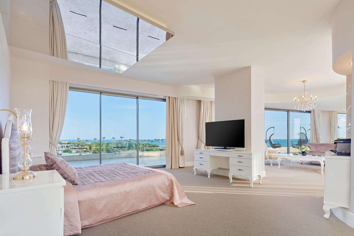 A spacious bedroom with a large bed, a TV, and a view of the ocean.