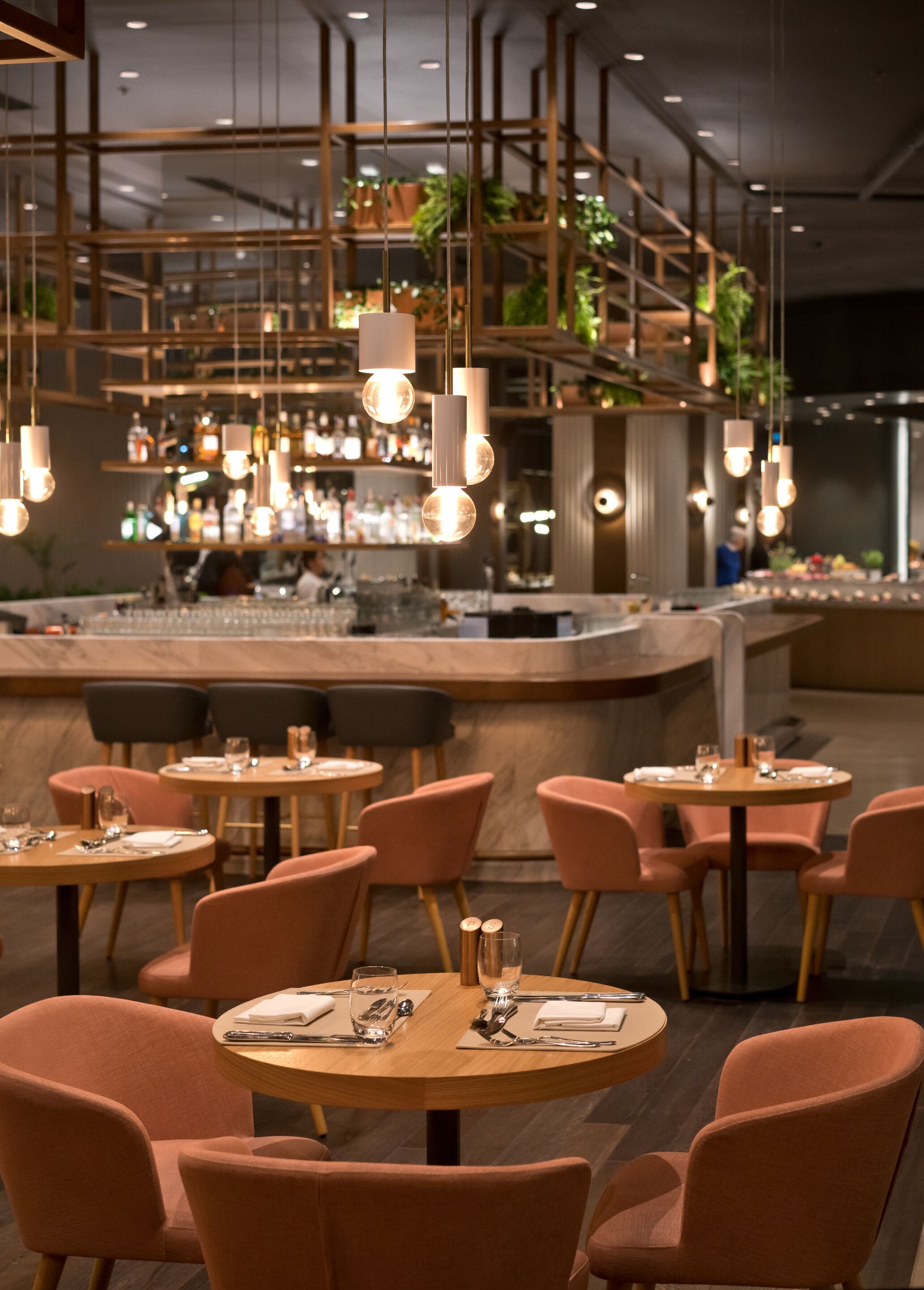 Un restaurant moderne avec des tables et des chaises rondes, des luminaires suspendus et un bar situé au fond de la salle.
