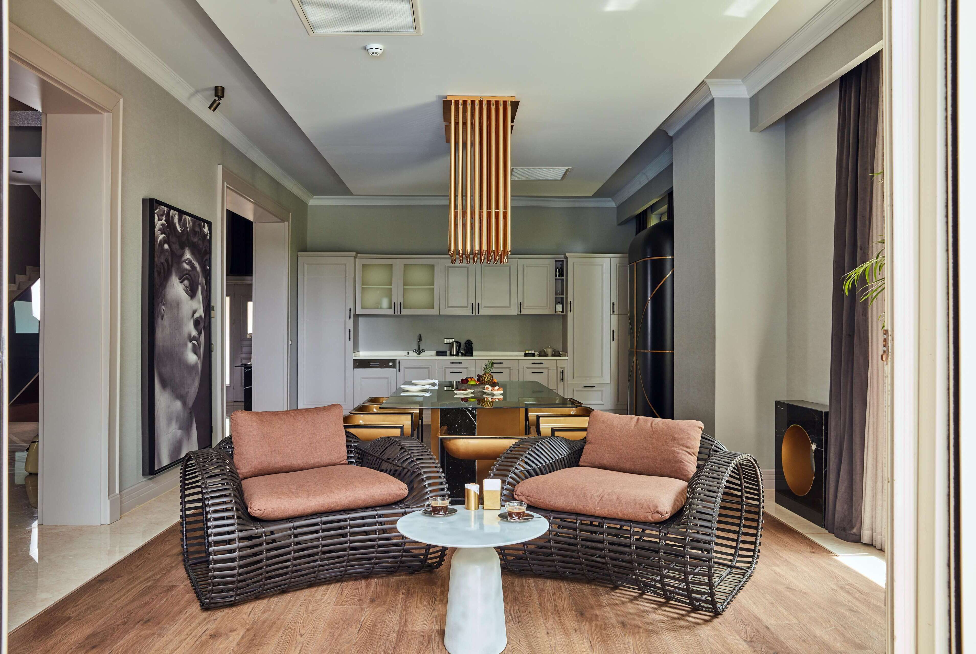 A modern living room with wicker furniture, a central coffee table, and a kitchen in the background.