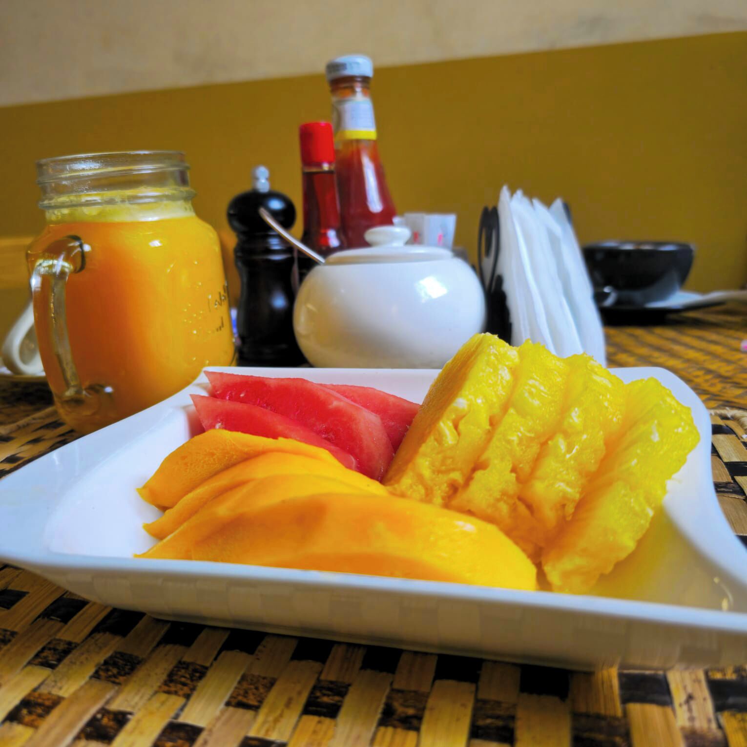 A breakfast plate with sliced fruits and a glass of orange juice.