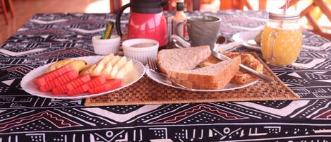 Une table dressée avec des aliments pour le petit-déjeuner, notamment des tartines, de la confiture et une carafe de jus d’orange.
