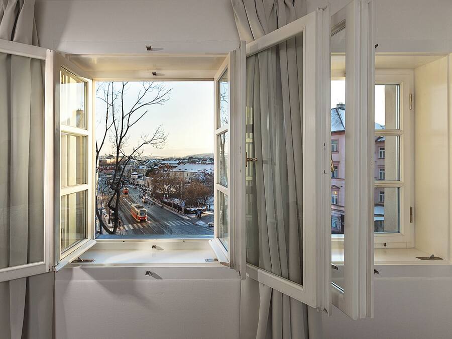 Una habitación con amplios ventanales, vista a una calle nevada y edificios, y una puerta visible.