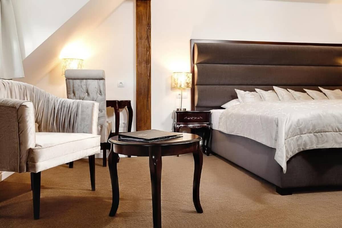 A hotel room with a large bed, a chair, a small table, and two bedside lamps.