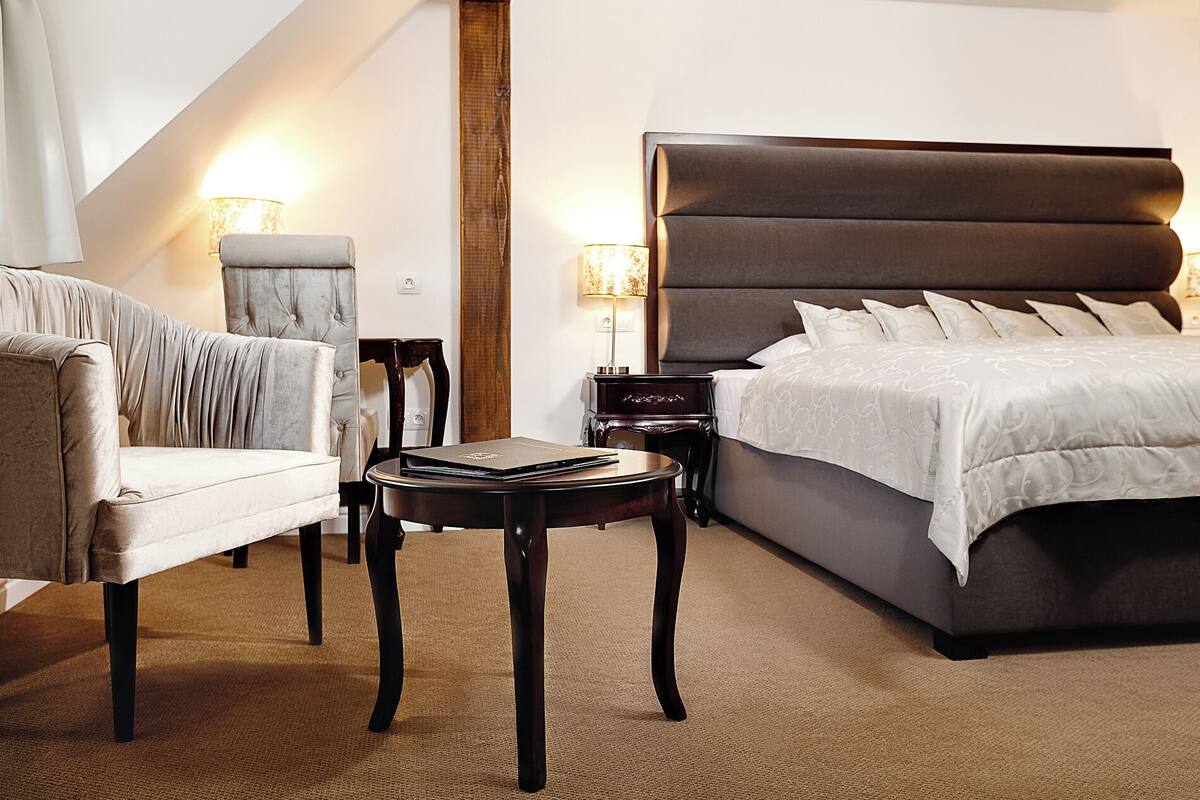 A hotel room with a large bed, a chair, a small table, and two bedside lamps.