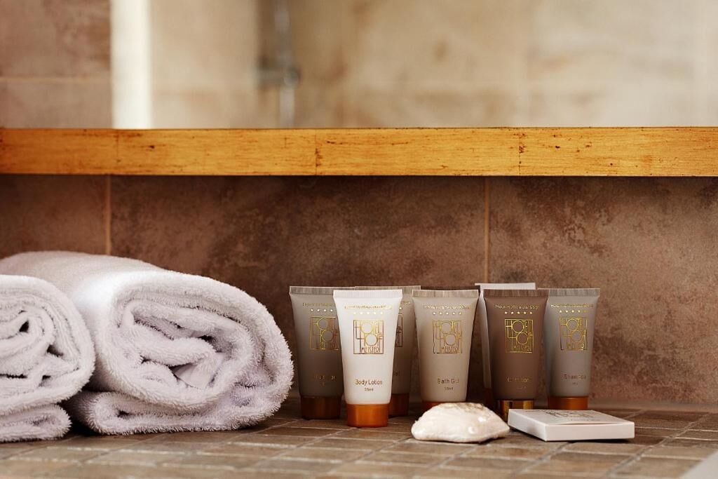 A bathroom with a wooden shelf holding rolled towels and various toiletries.