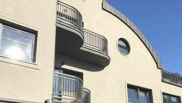 A multi-story building with balconies, a cafe area with outdoor seating, and a clear blue sky.
