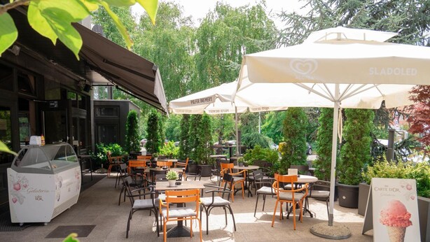Un área de café al aire libre con mesas, sillas, sombrillas y una vitrina de helados.