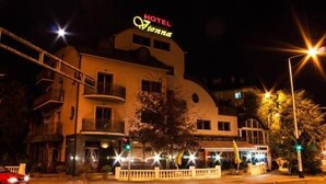 Un hotel llamado "HOTEL Aionna" con un letrero llamativo, un balcón en el segundo piso y vista a la calle con semáforos y un paso de peatones.