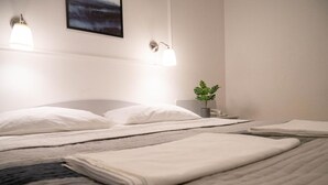 Un cuarto de hotel con una cama bien hecha, dos lámparas de noche, una pequeña planta en maceta y un cuadro en la pared.