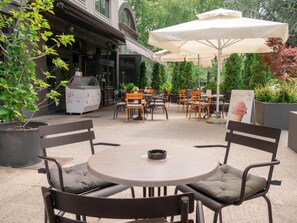 An outdoor patio with round tables and chairs, a large umbrella, and a menu stand. - Hotel Vienna (Zagreb)