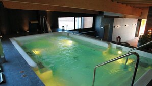 An indoor swimming pool with clear water, a metal ladder, and a view of the outside through large windows. - Isla Bella (Arnuero)