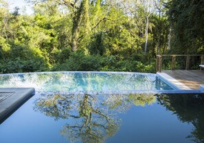 A clear swimming pool surrounded by dense greenery, with a wooden deck and a metal railing. - Mocona Virgin Lodge (El Soberbio)