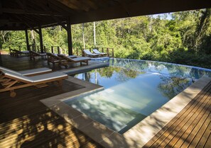 A clear view of a swimming pool with wooden deck and lounge chairs, surrounded by lush greenery. - Mocona Virgin Lodge (El Soberbio)
