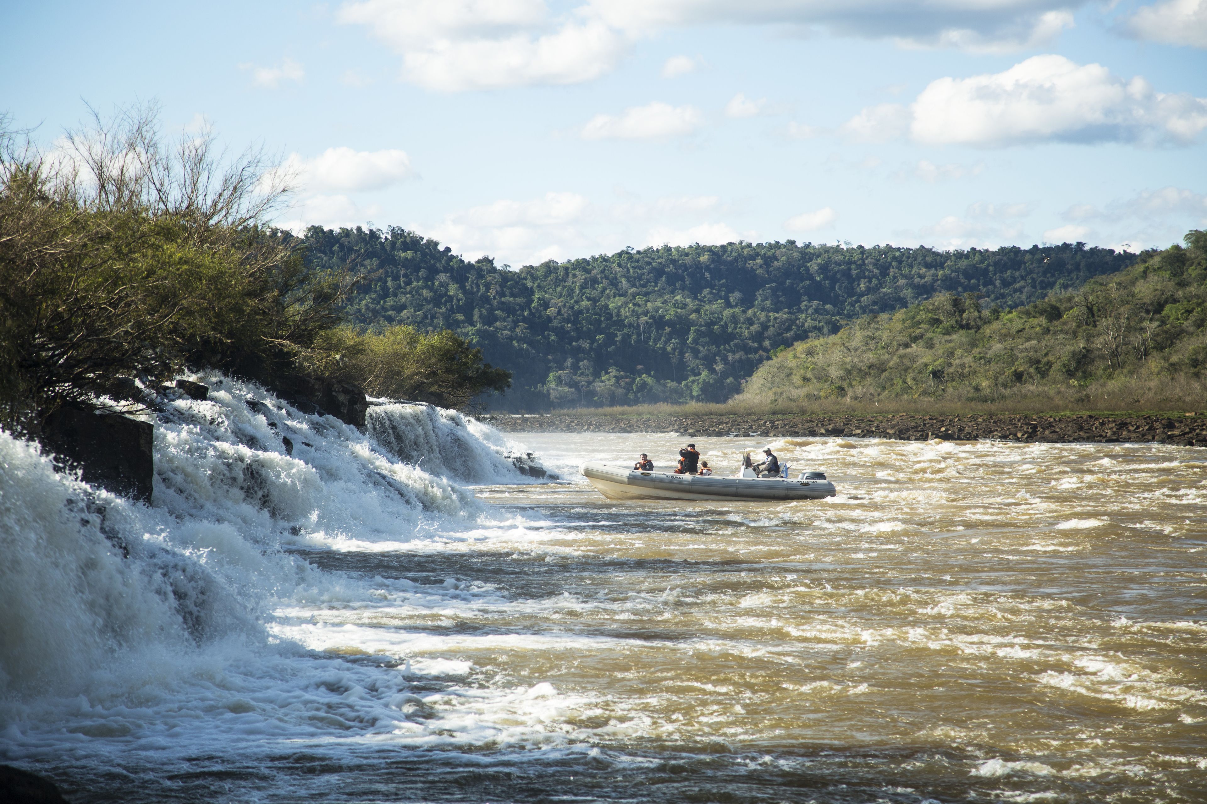 A river with a waterfall and a boat with people.