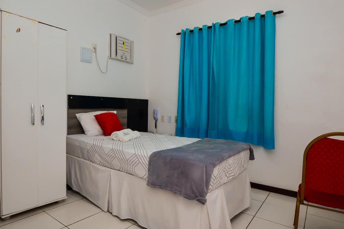 A hotel room with a bed, a wardrobe, a desk, a chair, and a window with curtains.