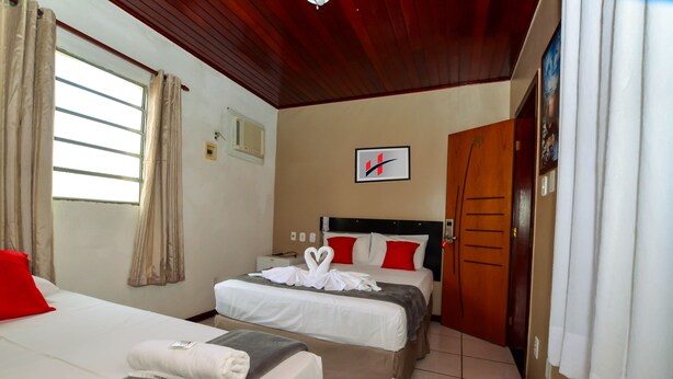 A hotel room with two beds, a wooden ceiling, a framed picture on the wall, and a door with a wooden panel. - Hotel Diamante Negro - Salvador (Salvador)