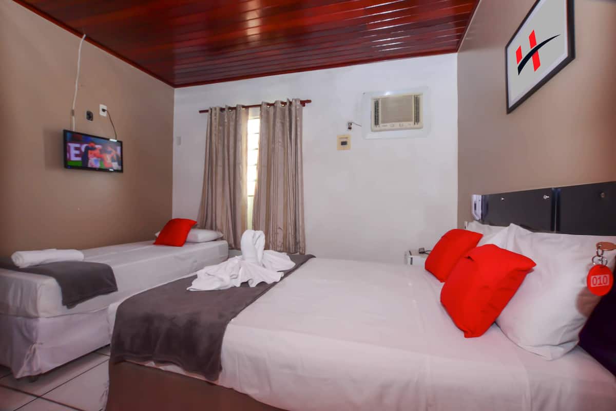 A hotel room with two beds, a TV, a window with curtains, and a ceiling with wooden beams.