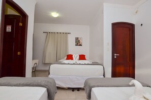 Habitación de hotel con dos camas, una puerta de madera, una pared blanca, una cortina y un cuadro pequeño.