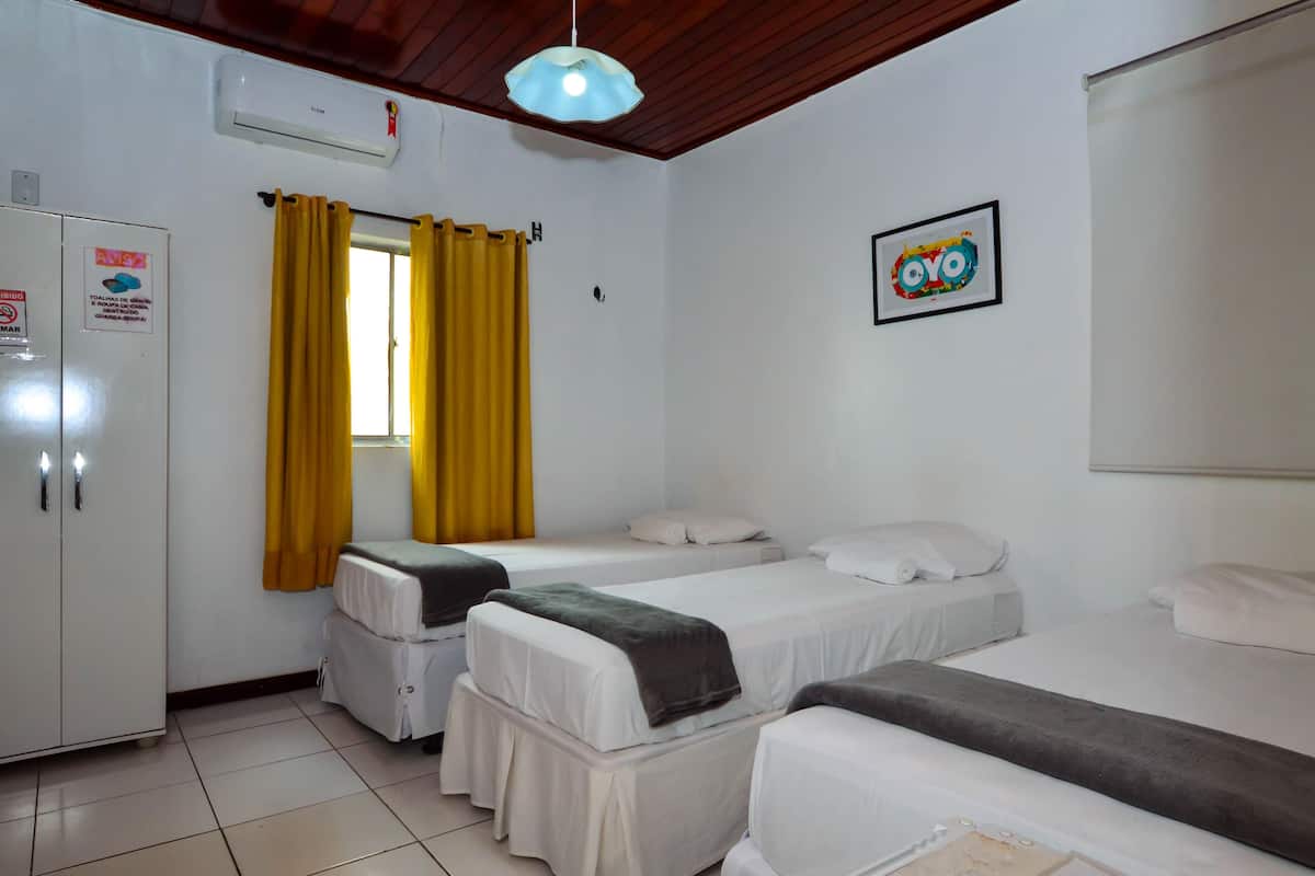 A hotel room with two single beds, a wardrobe, a window with yellow curtains, and a ceiling fan.