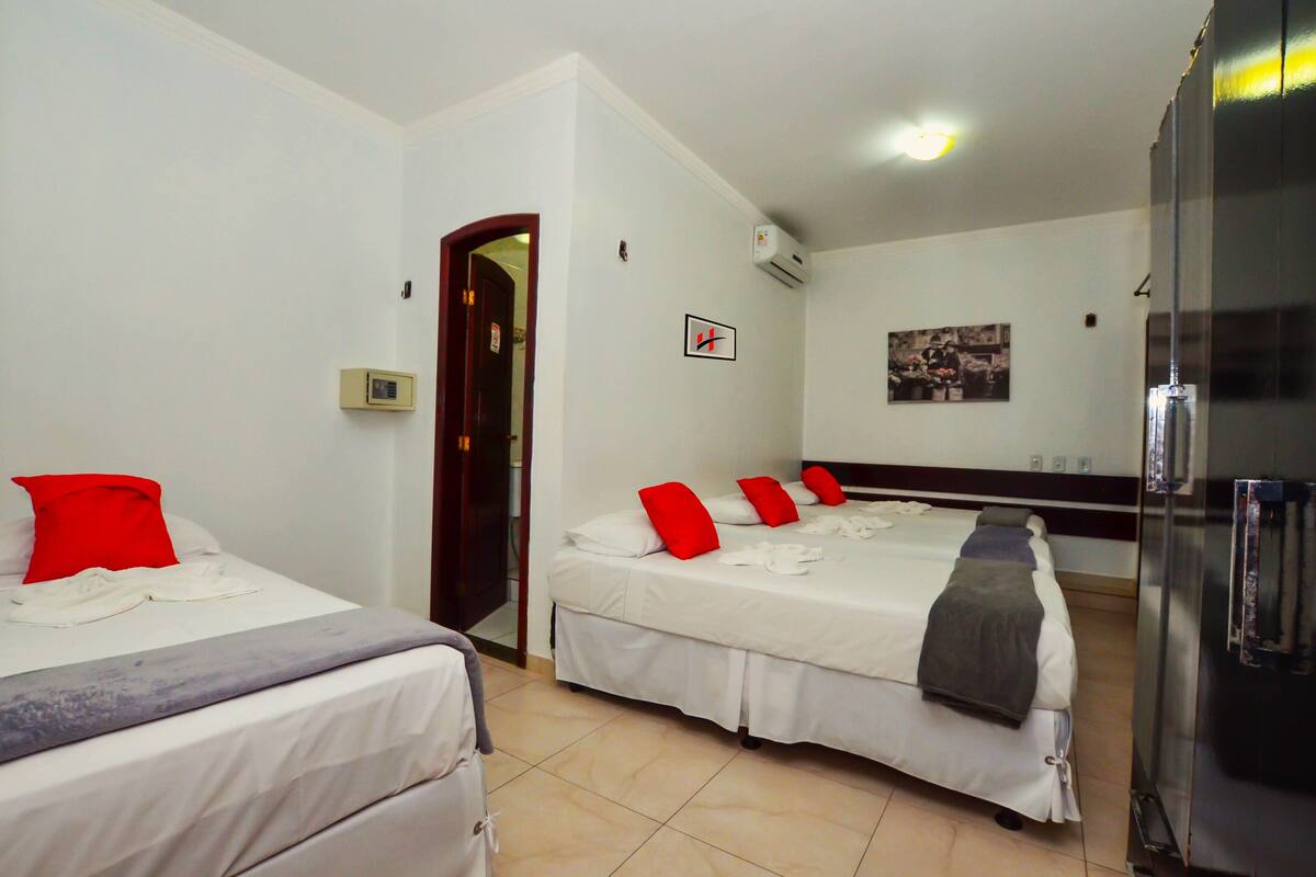 A hotel room with two beds, a refrigerator, a door, and a wall-mounted air conditioner.