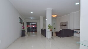 A spacious hotel lobby with a reception desk, a seating area with a sofa, a potted plant, and a chandelier. - Hotel Diamante Negro - Salvador (Salvador)