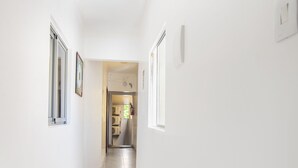 A narrow, well-lit hallway with white walls and tiled flooring, leading to a room with a refrigerator and a window. - Hotel Diamante Negro - Salvador (Salvador)