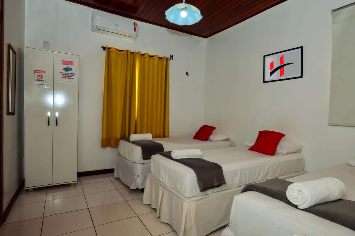 A hotel room with two single beds, a wardrobe, a ceiling fan, and a wall-mounted air conditioner.