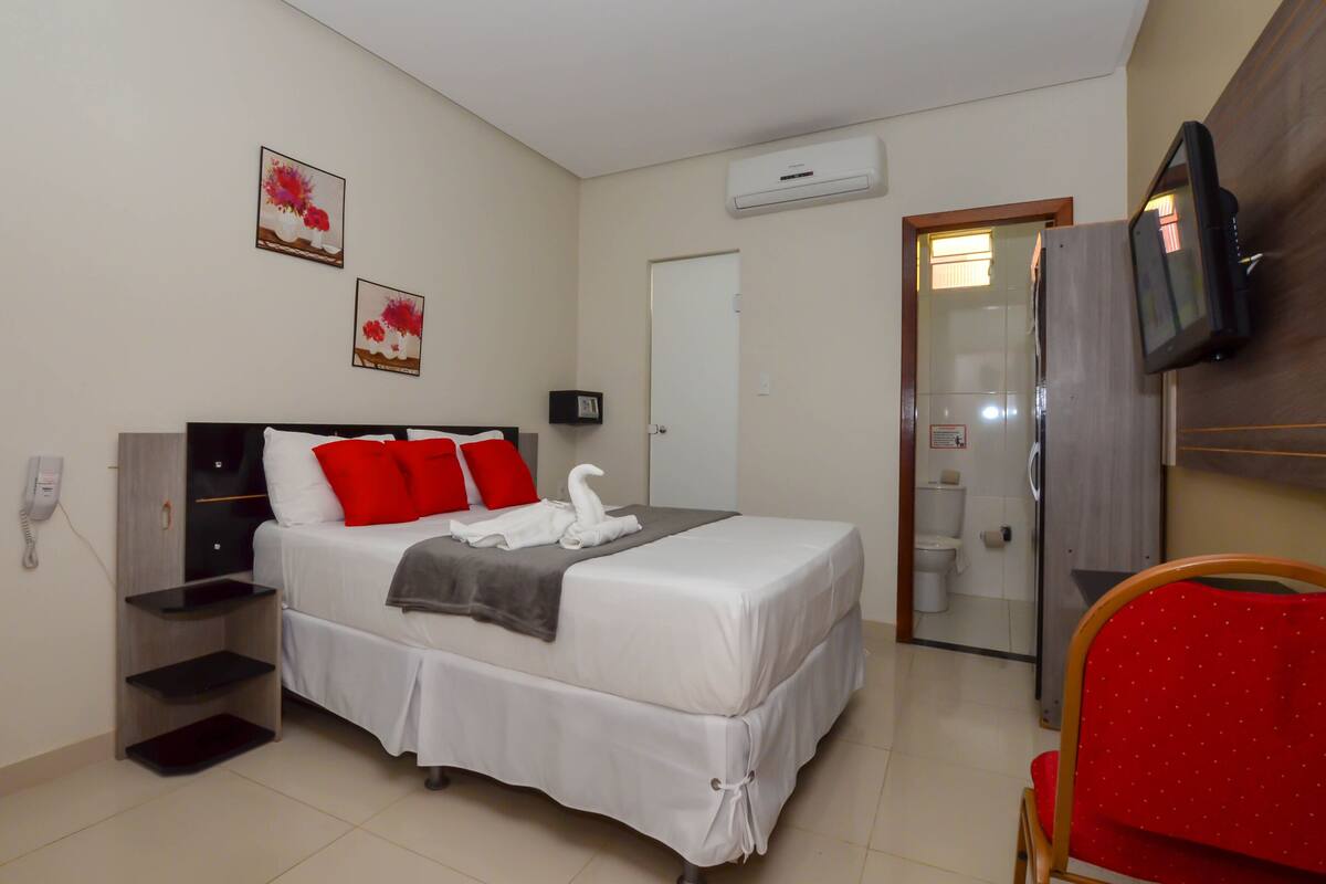 A hotel room with a bed, a TV, a phone, and a shower area.