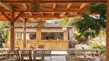 Une terrasse extérieure avec des meubles en osier et un coin bar à l’arrière-plan.