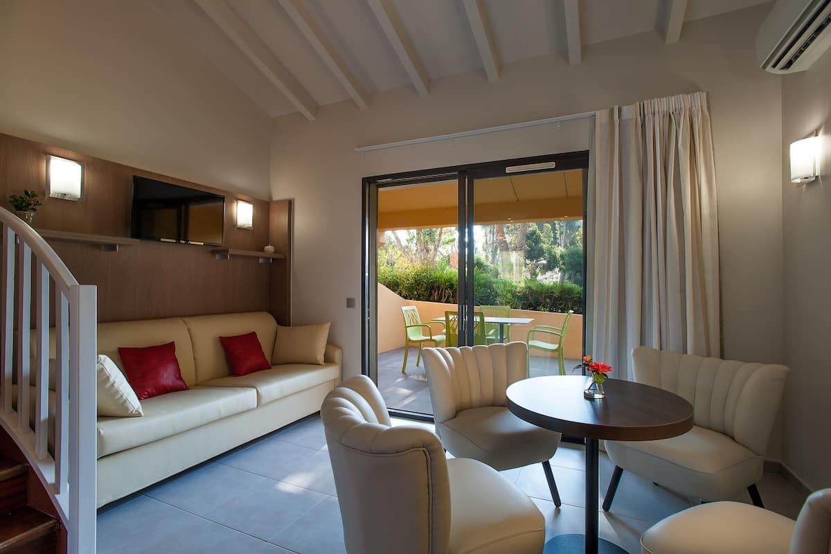 Una sala moderna con un sofá, sillones y una mesita. Hay un ventanal corredero que da a un espacio exterior con sillas y una mesa.