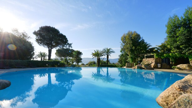 A clear blue pool surrounded by rocks and trees, with a view of the sea in the background. - Hotel Marina Corsica (Porto-Vecchio)
