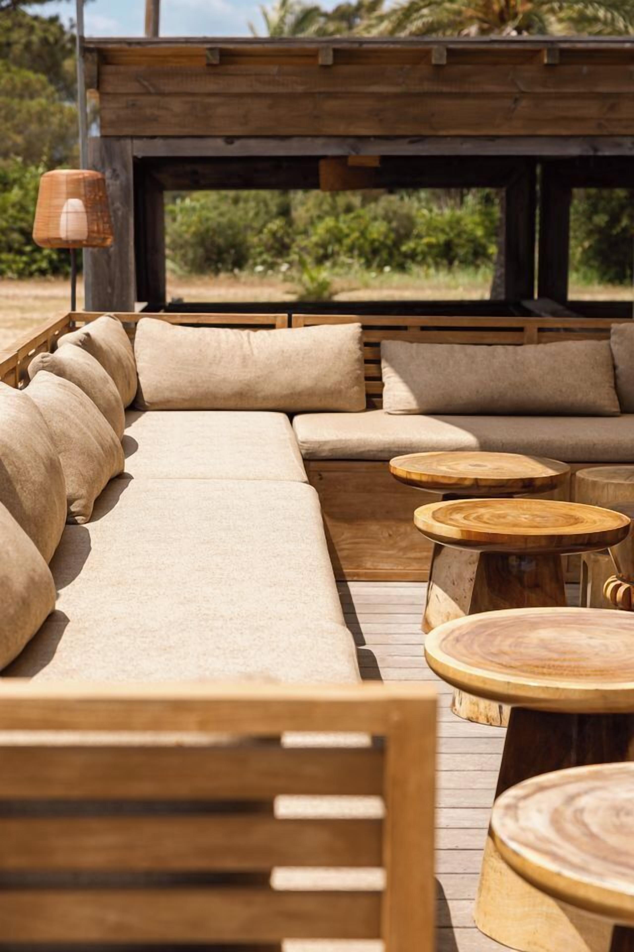 A wooden deck with a sofa, round wooden tables, and a lamp.
