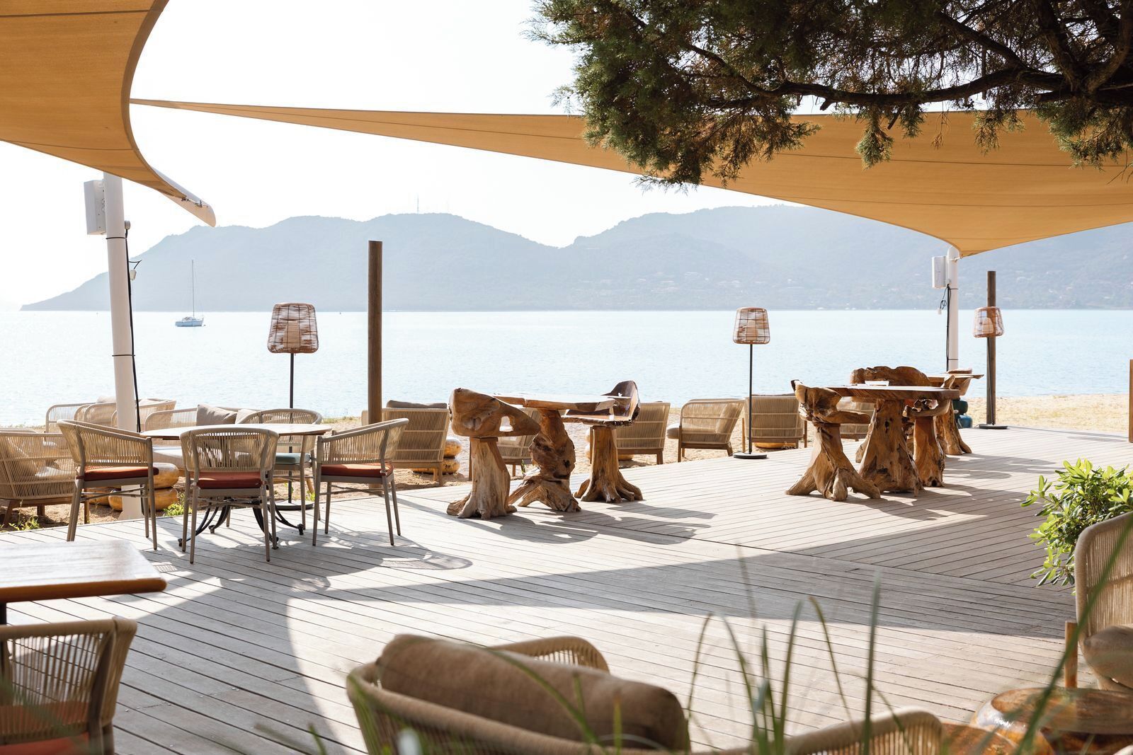 Une terrasse en bois, agrémentée de meubles en osier et d’une table, qui offre une vue sur une étendue d’eau, avec des montagnes en arrière-plan.