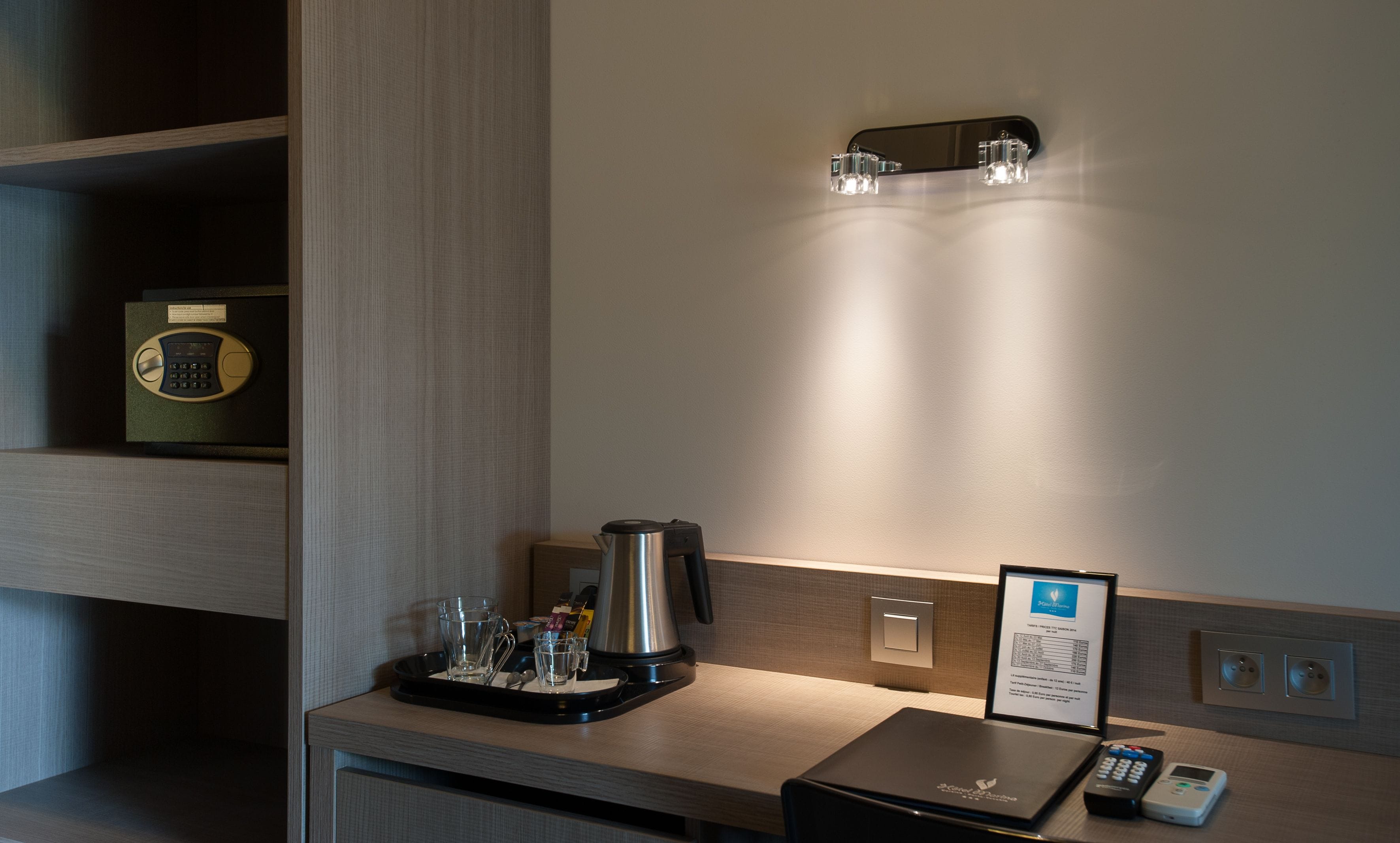 A hotel room with a coffee maker, a scale, a tray with glasses, and a remote control.