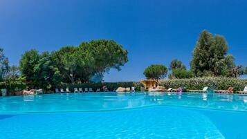 A clear blue swimming pool surrounded by lounge chairs and trees.