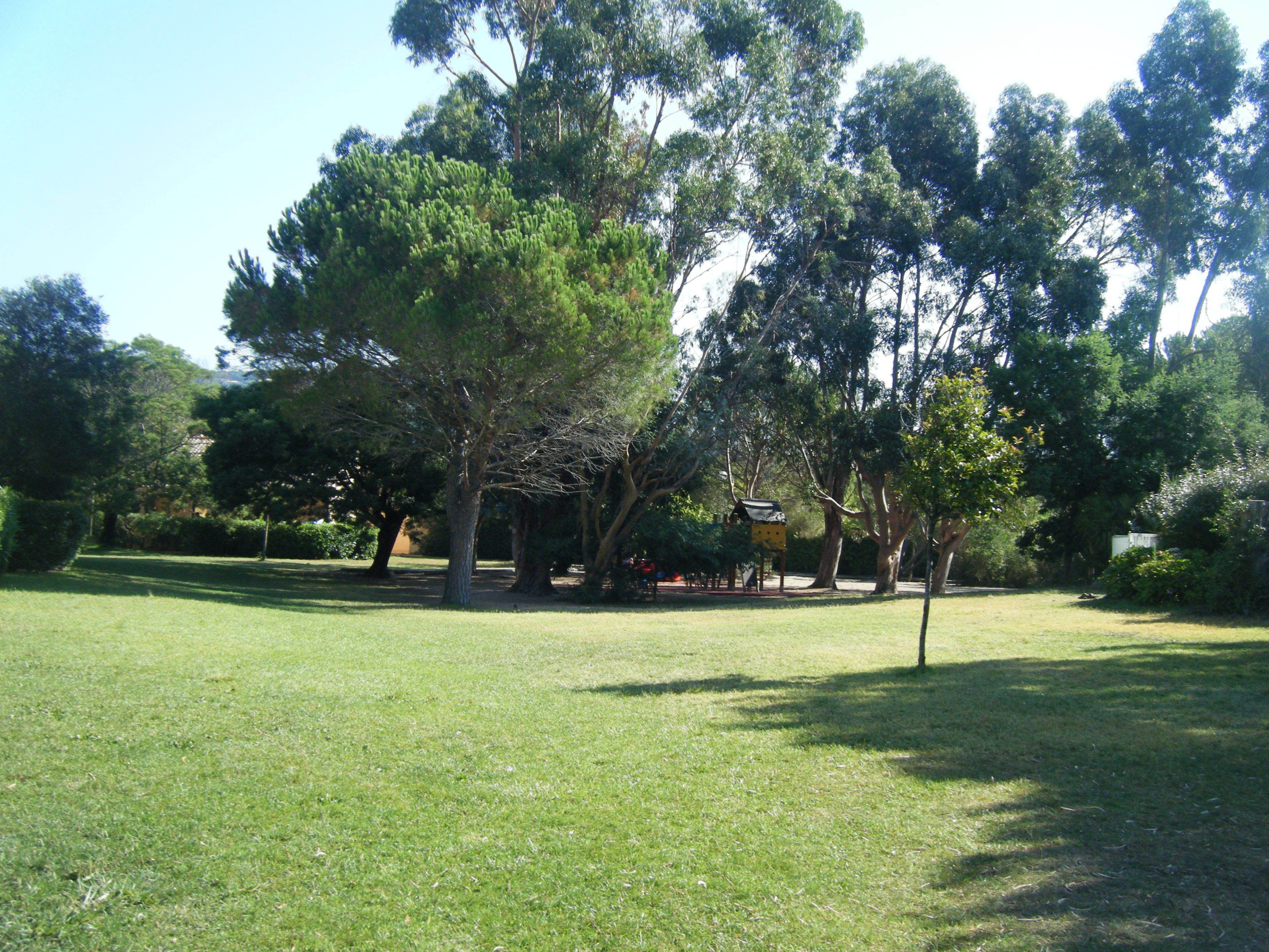 Un parco con un’area verde, alberi e una piccola costruzione.