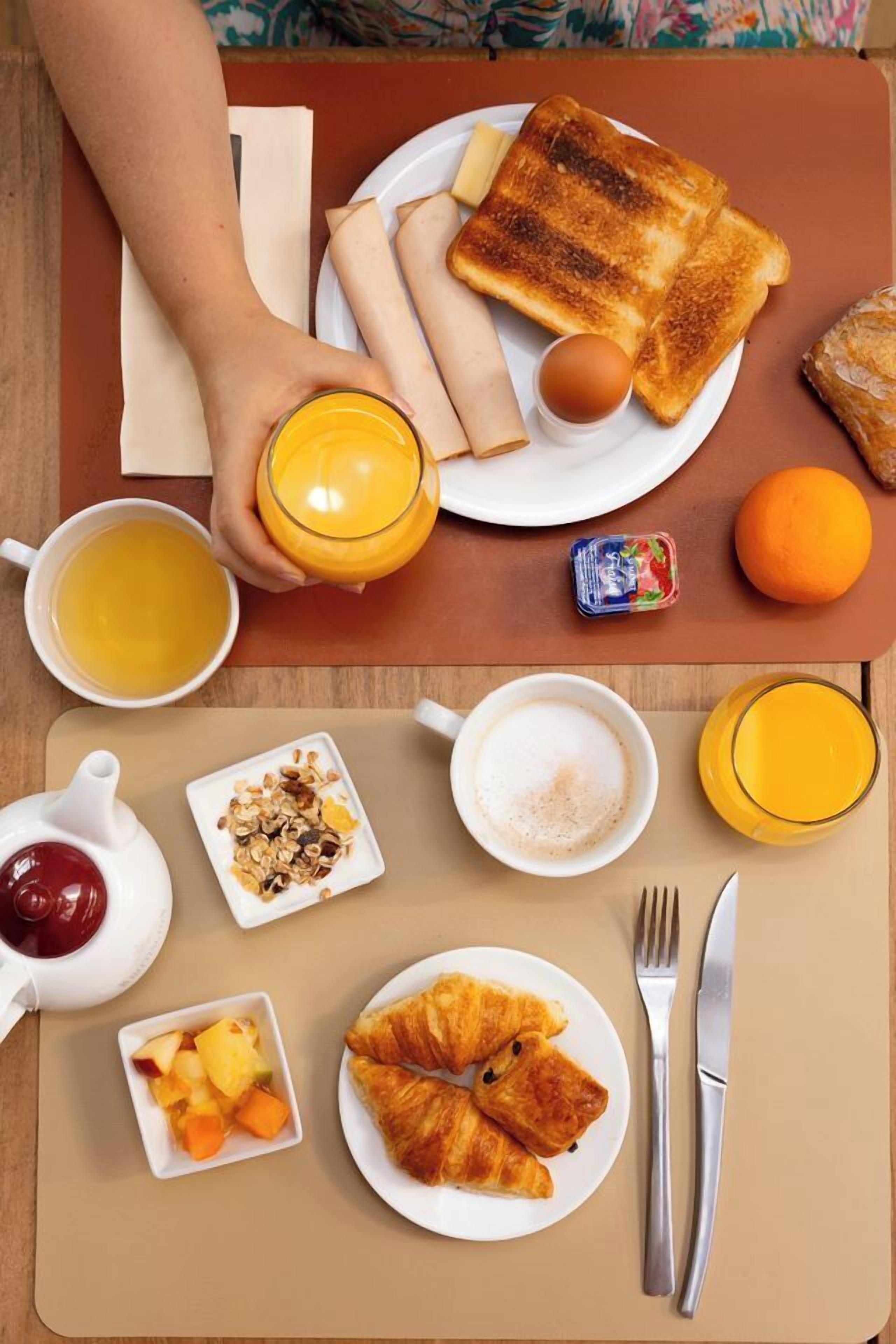 Une table de petit-déjeuner avec des toasts, des œufs, du jus d’orange, un croissant et un saladier de fruits.