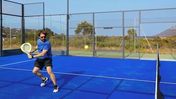 A tennis court with a player in action, a net, and a clear sky in the background.