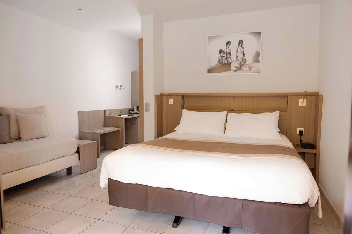 Una habitación de hotel con una cama grande, un sofá, un escritorio y un cuadro colgado en la pared.