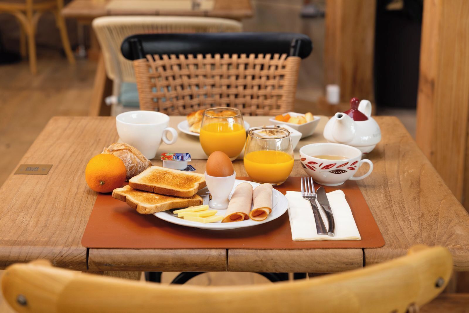 A breakfast table with toast, eggs, orange juice, and a teapot.