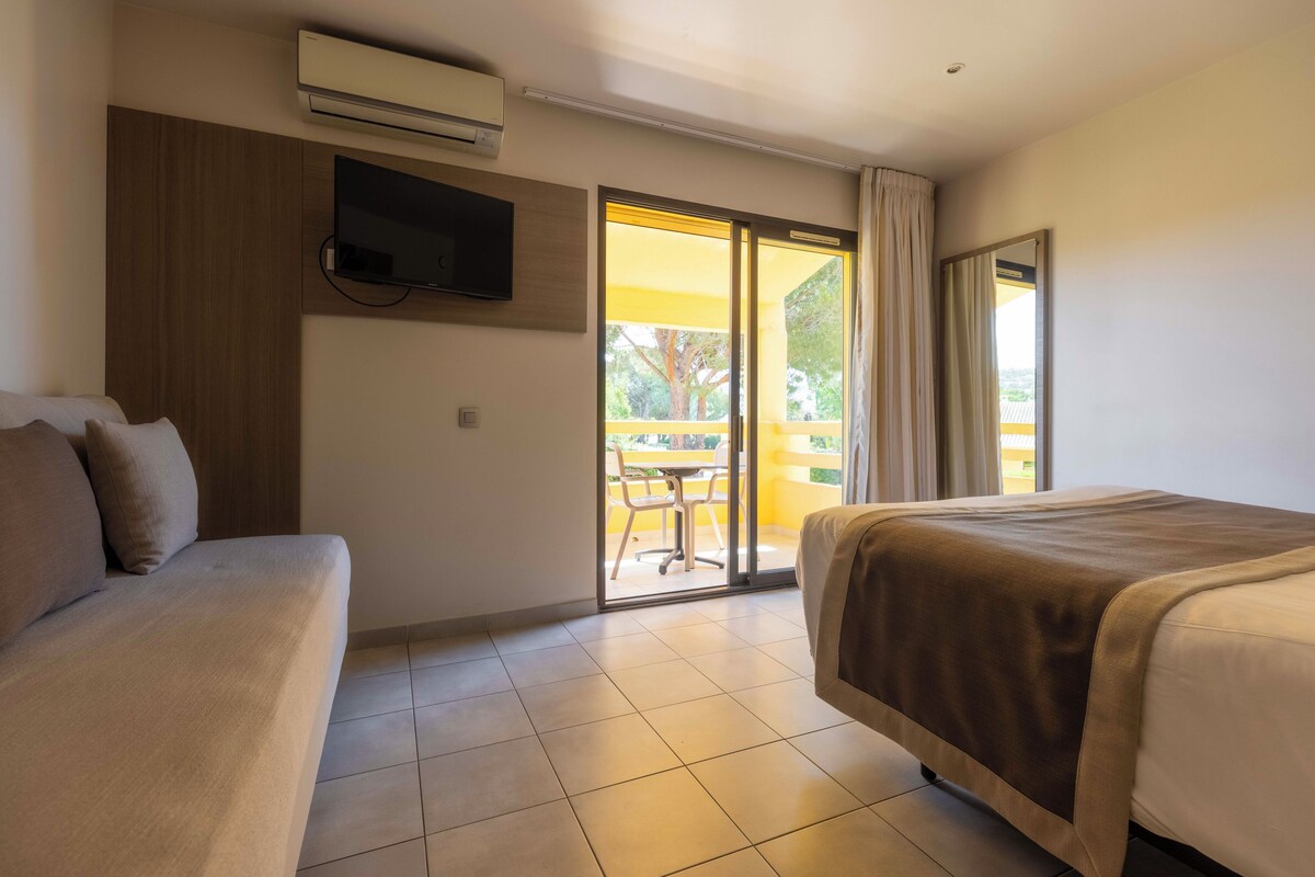 Een hotelkamer met een bed, een slaapbank, een aan de muur bevestigde televisie en een schuifdeur naar een buitengebied.